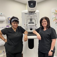 Picture of two females who work in the Mammography Department. One of them is taking a selfie and the other one is in her scrubs standing in front of 3-D Mammography Equipment at Russell County Hospital Women's Health Center