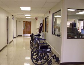 Picture of the emergency department hallway. There is wheelchairs and windows with offices